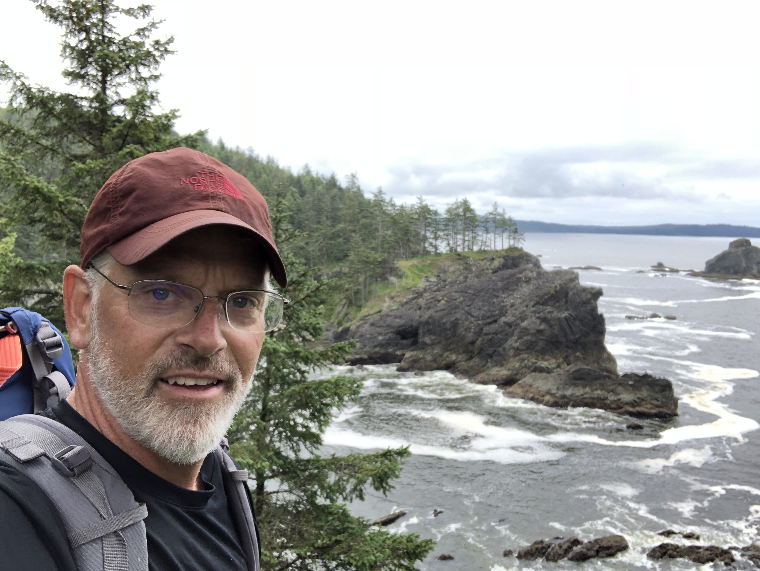 Brendan C Curran, host of Trails and TNT podcast, stands at the ocean in the Pacific Northwest